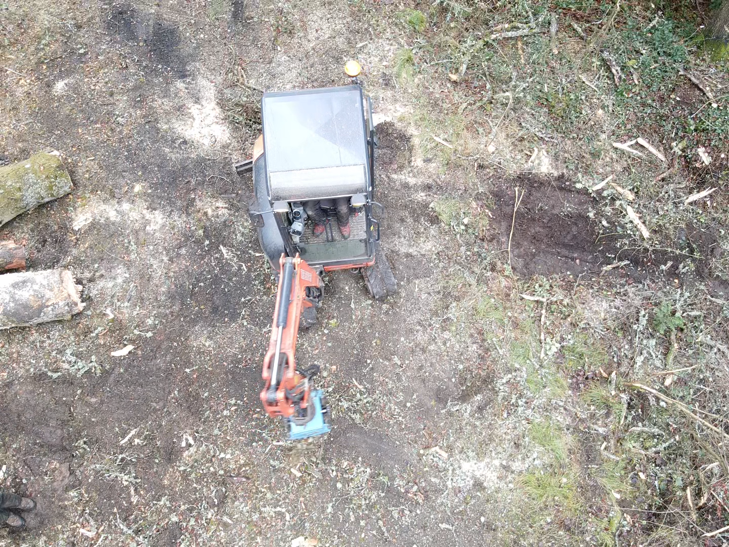 Aerial view of an excavator fitted with a grapple attachment working in a cleared plot.