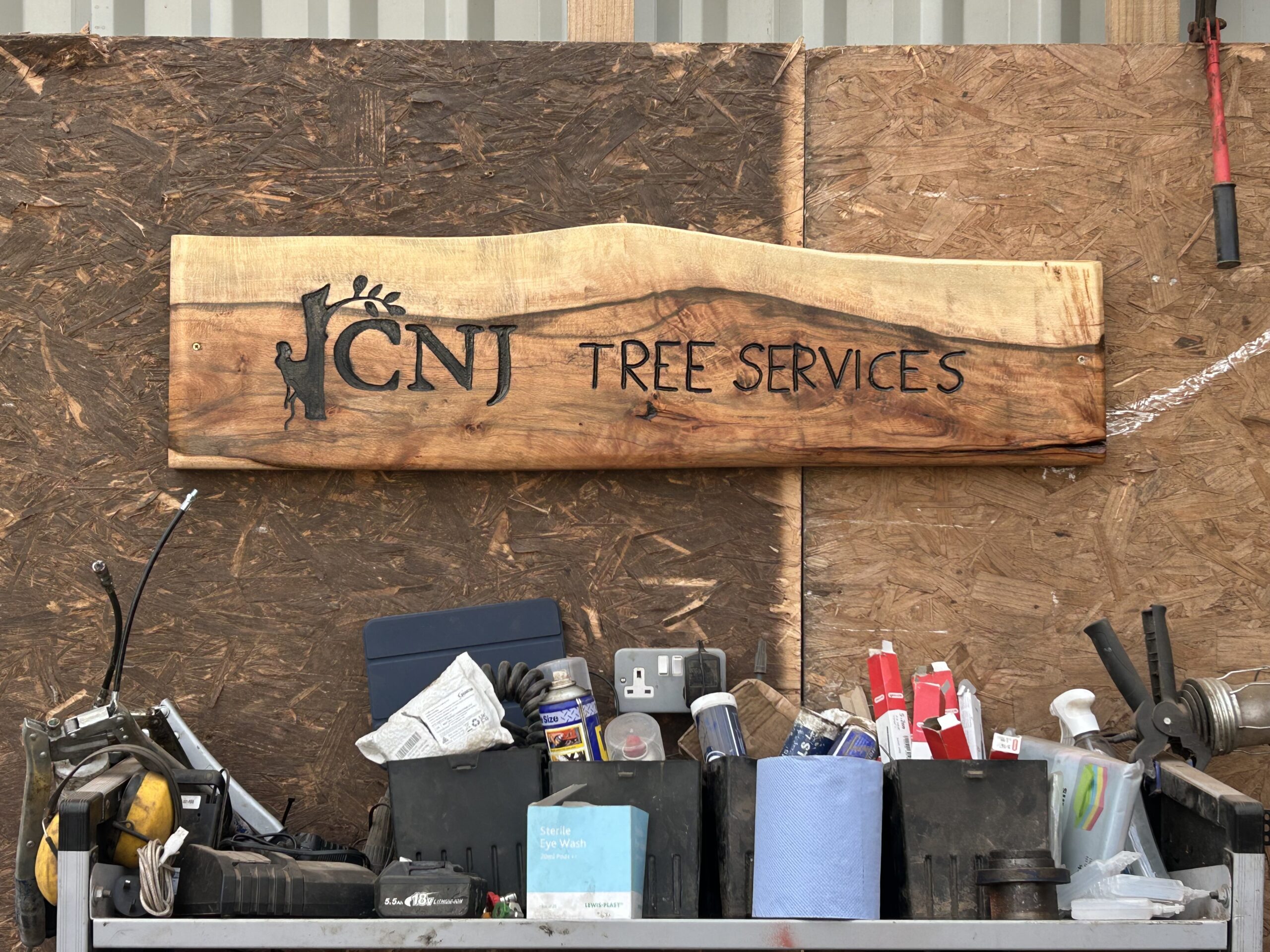 A carved wooden CNJ Tree Services sign displayed in a workshop.