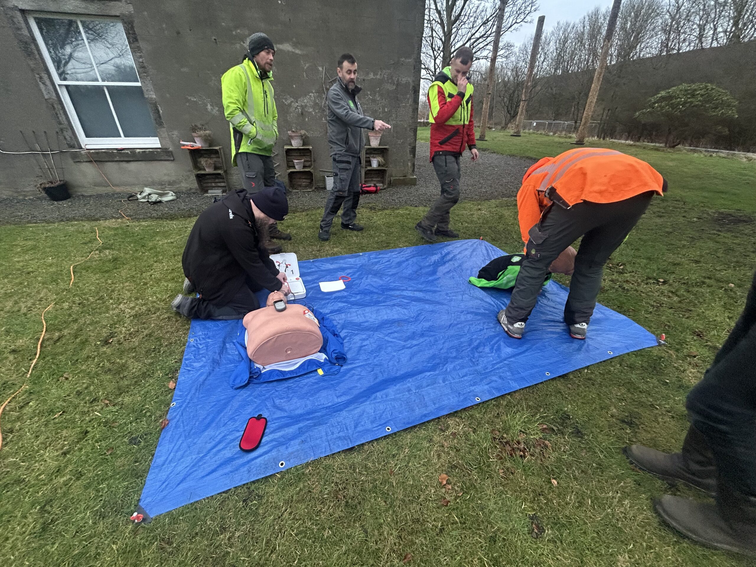 A tree surgery team practicing CPR on a training mannequin outdoors as part of safety training.