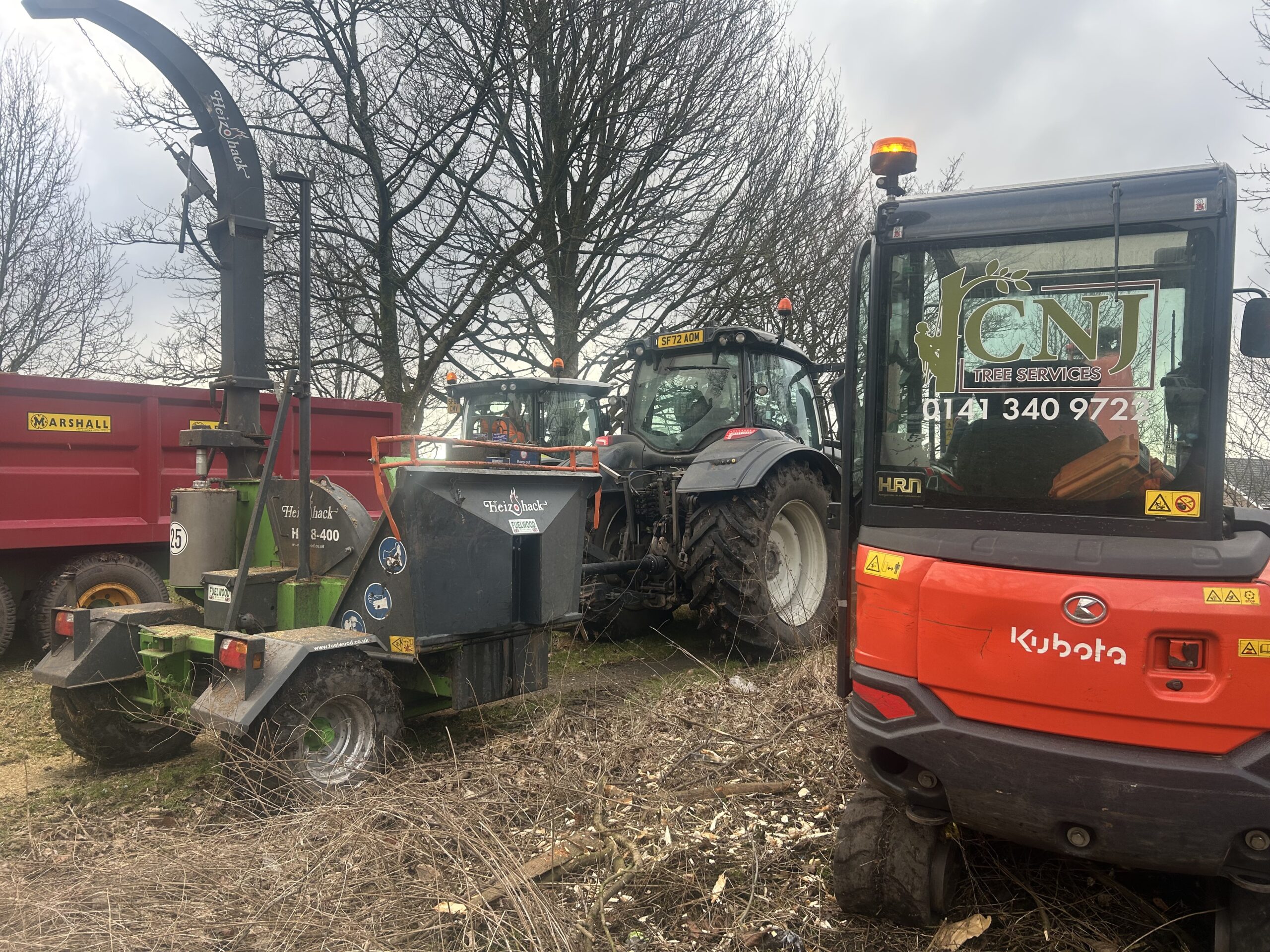 Two tractors and an orange wood chipper marked with tree service branding, parked ready for a commercial job.