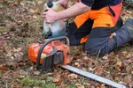 worker kneeling with chainsaw among fallen leaves